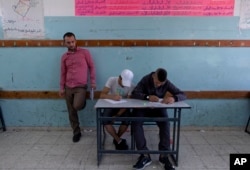 In this Sunday, May 26, 2019 photo, a teacher supervises while two Palestinian school children attend a final exam at the United Nations Relief and Works Agency for Palestine Refugees in the Near East, UNRWA, Hebron Boys School.