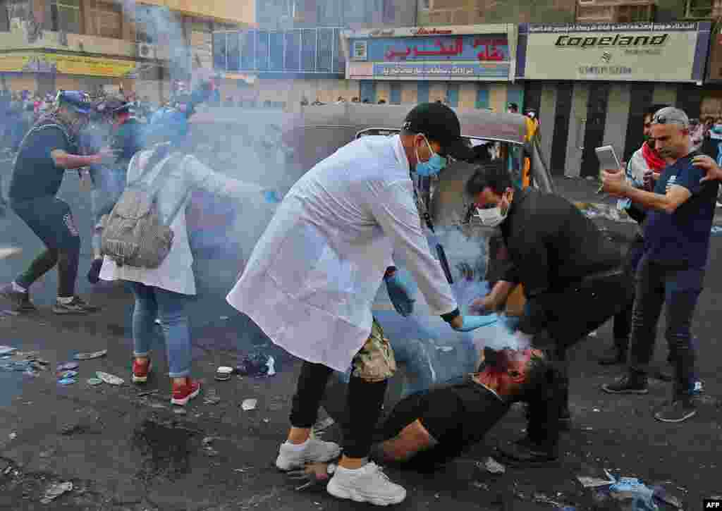 Iraqi volunteers help a protester who was struck by a tear gas canister fired by security forces at Baghdad&#39;s Khallani square during ongoing anti-government demonstrations.