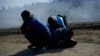 Three Honduran migrants huddle in the riverbank amid tear gas fired by U.S. agents on the Mexico-U.S. border after they and a group of migrants got past Mexican police at the Chaparral border crossing in Tijuana, Mexico, Nov. 25, 2018. 