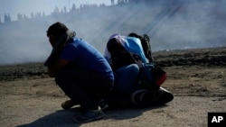 Three Honduran migrants huddle in the riverbank amid tear gas fired by U.S. agents on the Mexico-U.S. border after they and a group of migrants got past Mexican police at the Chaparral border crossing in Tijuana, Mexico, Nov. 25, 2018. 