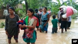 Warga desa Nepal membawa barang-barang mereka mengarungi jalan yang banjir di Bardia, Nepal barat (15/8). (AP/Bhabuk Yogi)