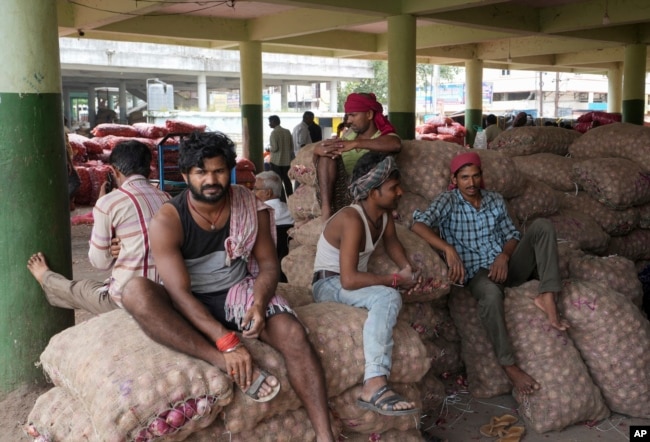 FILE - Workers rest on bags of onions at a wholesale market in Hyderabad, India, Friday, Aug. 5, 2022. (AP Photo/Mahesh Kumar A.)