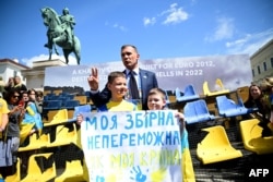 El presidente de la Asociación Ucraniana de Fútbol, Andriy Shevchenko, posa con niños que sostienen un cartel que dice "Mi selección nacional es tan invencible como mi país" frente a asientos dañados en el estadio de Járkov, Ucrania, el 17 de junio de 2024.