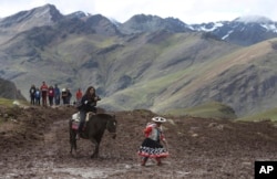 In this March 2, 2018 photo, a tourist ride a horse led by an Andean guide to Rainbow Mountain, a ridge of multicolored sediments laid down millions of years ago and pushed up as tectonic plates clashed, in Pitumarca, Peru. (AP Photo/Martin Mejia)