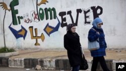 FILE - Women walk pass graffiti that reads "Freedom for Ever" on the outskirts of Idlib, north Syria. 