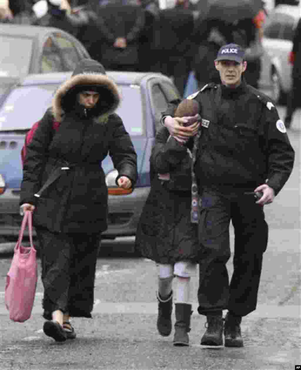 A student, center, flanked by an unidentified woman and a police officer leave a Jewish school where a gunman opened fire killing four people in Toulouse, southwestern France, Monday, March 19, 2012. A father and his two sons were among four people who di