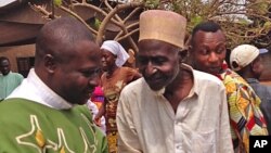 FILE - Father Justin Nary, left, greets Ousmane Mahamat, one of the 800 Muslims seeking refuge in a Catholic church in Carnot a town 200 kilometers (125 miles) from the Cameroonian border in Central African Republic, Feb. 23, 2014.