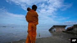Ranajit Mandal, 35, the priest of a temple of Hindu goddess Durga stands with his son watching the temple being washed away by the river Brahmaputra at Murkata village, northeastern Assam state, India, Thursday, Oct. 13, 2022. 