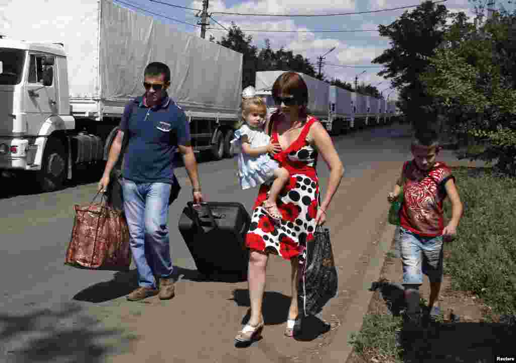 Refugees walk past a Russian humanitarian aid convoy near a Russia-Ukraine border crossing point, in Rostov region, Aug. 21, 2014.