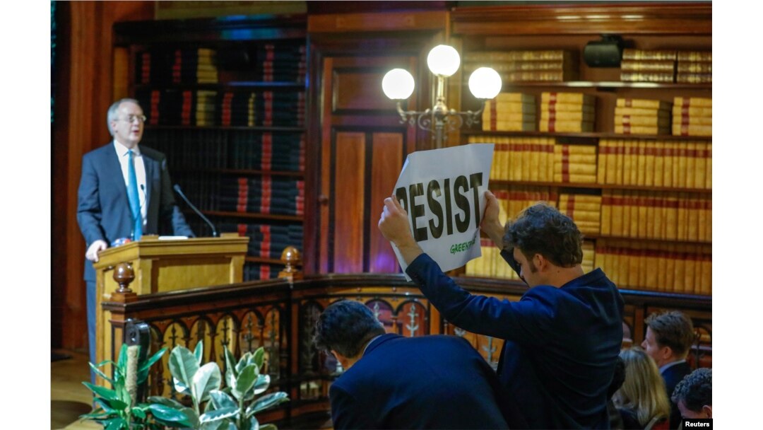 An environmental activist holds a banner reading "resist" while attending a speech by Myron Ebell, left, who leads U.S. President Donald Trump's Environmental Protection Agency's transition team, in Brussels, Belgium, Feb. 1, 2017.