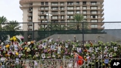 In this Wednesday, June 30, 2021, file photo, an unidentified woman visits the memorial wall full of photos of the missing and messages of love, support and prayers (David Santiago/Miami Herald via AP, File) 