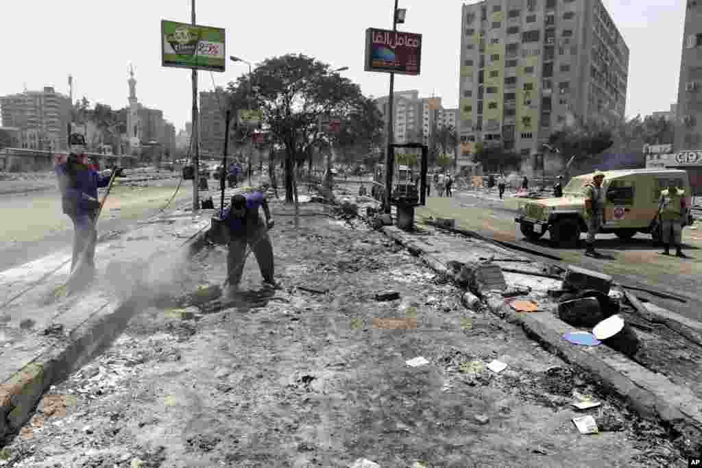 Egyptian government employees clean up as members of the Egyptians Army stand guard alongside the smoldering remains of the largest protest camp of Morsi supporters, Nasr City, Cairo, August 15, 2013.