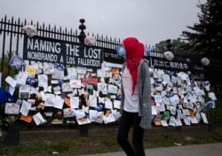 A woman passes a fence outside Brooklyn's Green-Wood Cemetery adorned with tributes to victims of COVID-19, May 28, 2020, in New York.