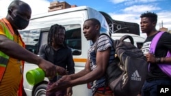 FILE - A taxi marshall wearing a face mask sprays sanitizer on passengers' hands to protect against coronavirus, at a minibus taxi station in Johannesburg, South Africa, March 26, 2020.