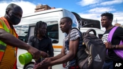 FILE - A taxi marshall wearing a face mask sprays sanitizer on passengers' hands to protect against coronavirus, at a minibus taxi station in Johannesburg, South Africa, March 26, 2020.