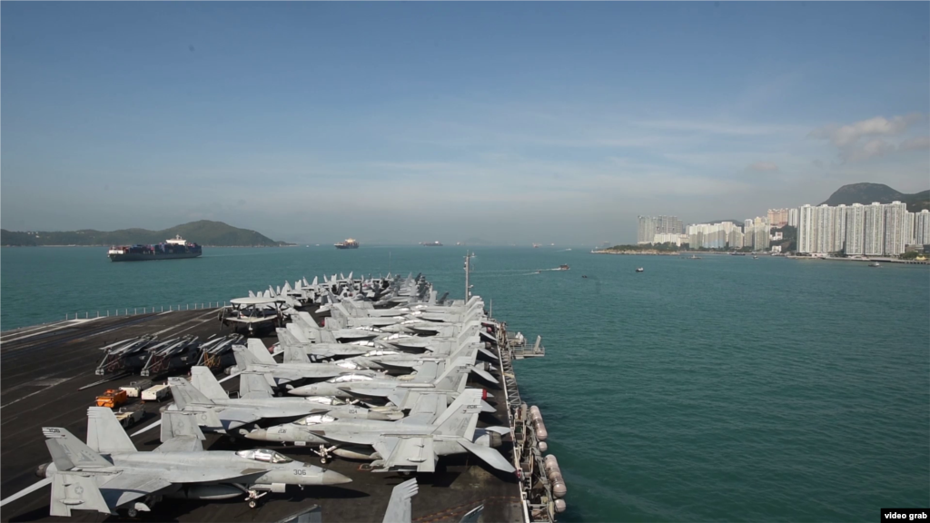 2018年11月下旬， 美国航空母舰里根号在香港水域停泊，甲板上飞机密列成行，远处港岛高楼在望。