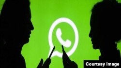 Deux silhouettes devant le logo de WhatsApp, le service de messagerie de Facebook.