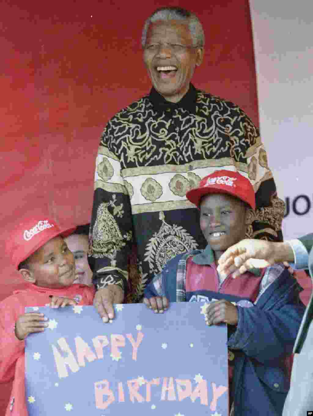 South African President Nelson Mandela celebrates the eve of his 77th birthday with two of the 2000 children present at a party on the grounds of Crown Mines in Johannesburg, where Mandela got his first job as a policeman. Childrens names unavailable.&nbsp;