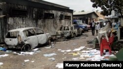 Des Congolais passent devant une maison et des véhicules qui ont brûlé lors des manifestations anti-gouvernement à Kinshasa, RDC, le 21 septembre 2016.