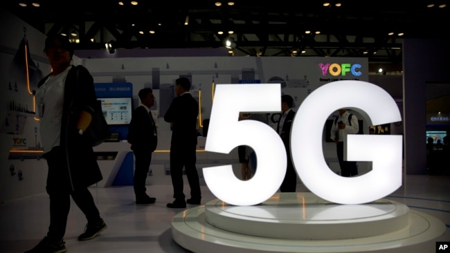 Visitors stand near a 5G logo at a display for Chinese fiber optic cable maker YOFC at the PT Expo in Beijing, Wednesday, Sept. 26, 2018. (AP Photo/Mark Schiefelbein)