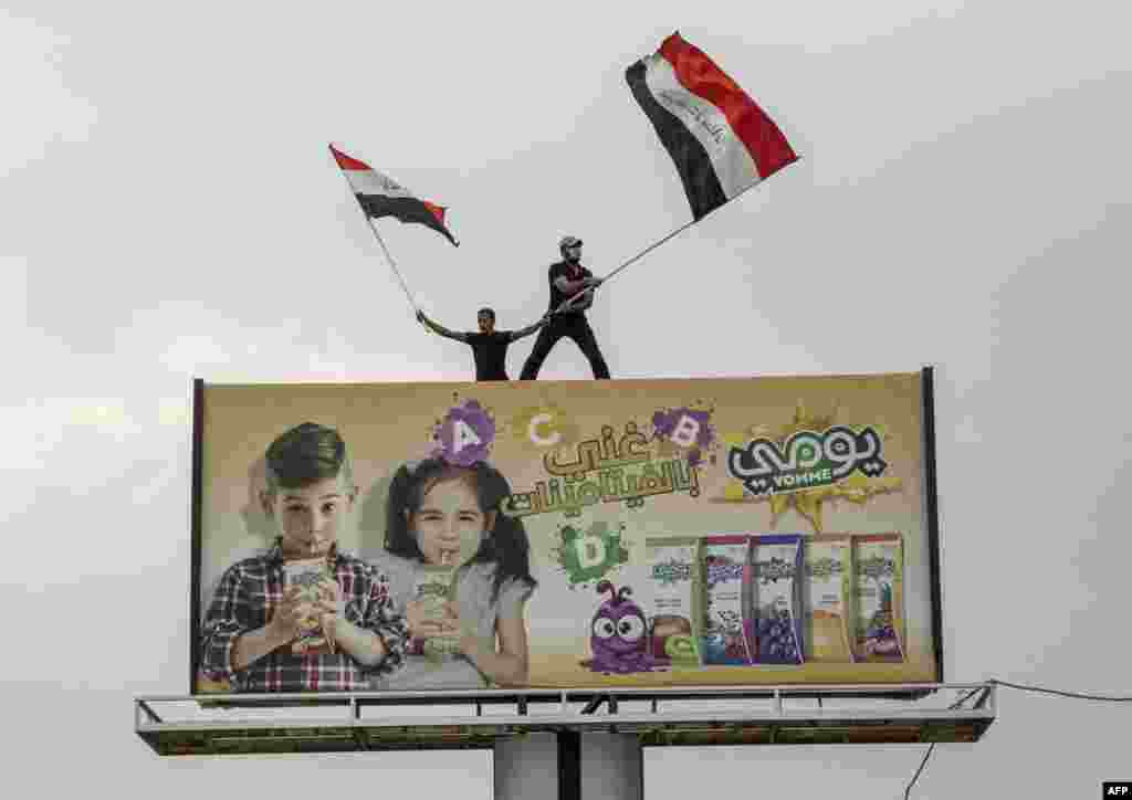 Iraqi protesters wave national flags as they stand on top of a billboard during an anti-government demonstration outside the local government headquarters in the southern city of Basra.