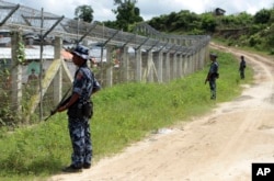 မြန်မာ-ဘင်္ဂလားဒေ့ရှ် နှစ်နိုင်ငံနယ်စပ်အကြားရှိ "no man's land" ကိုကာရံထားသည့် ခြံစည်းရိုးနားတွင် လုံခြုံရေးတာဝန်ယူထားသည့် မြန်မာ နယ်ခြားစောင့် တပ်ဖွဲ့ဝင်များ။ (တောင်ပြိုလက်ယာကျေးရွာအနီး၊ မောင်တောမြို့) (ဇွန် ၂၉၊ ၂၀၁၈)