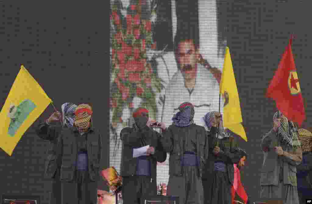 Masked supporters wave PKK flags in front of a screen showing jailed Kurdish rebel leader Abdullah Ocalan, Diyarbakir, Turkey, Thursday, March 21, 2013.