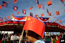 A Cambodian woman holds a Chinese flag as she walks a friendship bridge between Cambodia and China during its inauguration ceremony in Takhmao, Kandal provincial town, south of Phnom Penh, Cambodia, Monday, Aug. 3, 2015.