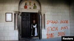 A monk stands next to graffiti sprayed on a wall at the entrance to the Latrun Monastery near Jerusalem, Sep. 4, 2012. 