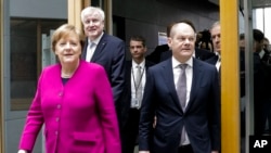 ນາຍົກລັດຖະມົນຕີແລະປະທານສະຫະພັນພັກປະຊາທິປະໄຕ ສາສະໜາຄຣິດ (Christian Democratic Union-CDU), ປະທານພັກ ທ່ານນາງ ແອງໂກລາ ເມີຣ໌ໂກ (Angela Merkel), ຊ້າຍ, ປະທານ ພັກສະຫະພັນສັງຄົມນິຍົມ ສາສະໜາຄຣິດ (Christian Social Union-CSU), ປະທານພັກ ທ່ານ ຮອສຕ໌ ຊີໂຮບເຟີ (Horst Seehofer), ທີ່ສອງຈາກຈາກຊ້າຍ, ແລະພັກສັງຄົມນິຍົມປະຊາທິປະໄຕ (Social Democratic Party-SPD) ຜູ້ນຳພັກຊົ່ວຄາວ ທ່ານໂອແລັຟ ຊໂກສ (Olaf Scholz), ຂວາ, ກຳລັງໄປຮອດໄປເຖິງກອງປະຊຸມຖະແຫຼງຂ່າວ, ໃນນະຄອນເບີລິນ, ເຢຍຣະມັນ, 12 ມີນາ 2018.