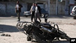 Palestinians walk near the debris of a damaged motorcycle after an Israeli airstrike in Deir al-Balah, central Gaza Strip, Sunday, Feb. 9, 2014. 