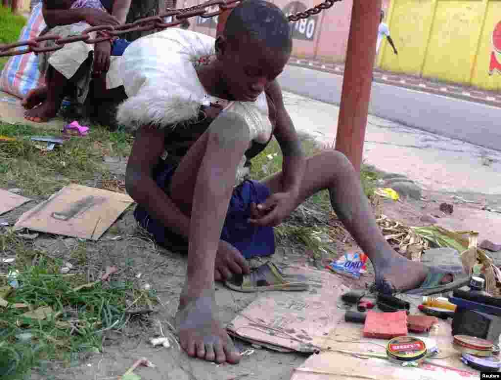 یک کودک آواره کنگویی در حال تعمیر کفش در خیابانی در کینشاسا - ژوئن ۲۰۱۳