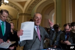 FILE - Senate Minority Leader Chuck Schumer of New York, joined by, from left, Sen. Ron Wyden, D-Ore., the ranking member of the Senate Finance Committee, and Sen. Debbie Stabenow, D-Mich., holds up a letter he sent to President Donald Trump, Senate Majority Leader Mitch McConnell of Kentucky, and Senate Finance Committee Chairman Sen. Orrin Hatch, requesting a bipartisan effort on tax reform, during a news conference on Capitol Hill, Washington, Aug. 1, 2017.