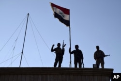 Iraqi soldiers plant the national flag over a government building in Ramadi as security forces advance their position in northern Ramadi, 70 miles (115 kilometers) west of Baghdad, Iraq, Dec. 21, 2015.