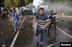 Migrants run as Hungarian riot police fires tear gas and water cannon at the border crossing with Serbia in Roszke, Hungary, Sept. 16, 2015.