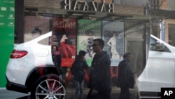 FILE - People are reflected on a window as they walk past fashion magazine posters near a Mercedes-Benz SUV on display at a showroom in Beijing, Oct. 26, 2015. Wealthy Chinese remain the No. 1 buyers of luxury products worldwide, according to a new study.