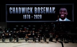 The Los Angeles Clippers kneel to pay respect to the Black Lives Matters movement while a photo of actor Chadwick Boseman is displayed on a screen being the team before their NBA first round playoff game against the Dallas Mavericks, Aug. 30, 2020.