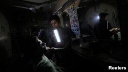 FILE - A barber holds a portable emergency light in his mouth while shaving a customer during a power outage at a low income neighborhood in Karachi, Pakistan, June 29, 2013. Pakistan faces a year-round electricity shortfall that hits around 7,000 megawatts in the summer.