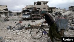 A man walks with his bicycle at a damaged site in the besieged town of Douma, eastern Ghouta, in Damascus, Syria March 30, 2018.