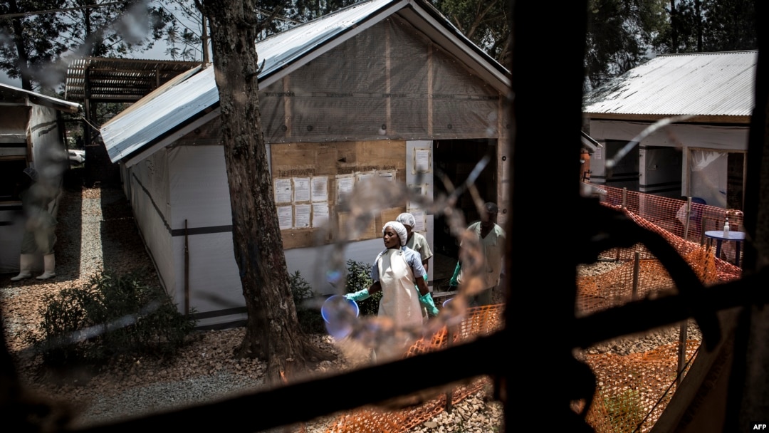 Pekerja kesehatan melihat dari lubang bekas tembakan di jendela sebuah pusat perawatan Ebola di Butembo, Republik Demokratik Kongo, 9 Maret 2019.