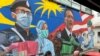 Sepasang suami istri Melayu makan siang di samping lukisan mural sebagai penghormatan untuk pekerja medis Malaysia dalam melawan virus corona Covid-19 di Damansara di Selangor, di luar Kuala Lumpur, Malaysia, 7 November 2020. (Foto: AP)