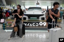 FILE - Passengers wait near a hybrid luxury SUV from China automaker Lynk&co displayed at the train station in Hangzhou in eastern China's Zhejiang province on Monday, July 3, 2023. (AP Photo/Ng Han Guan, File)