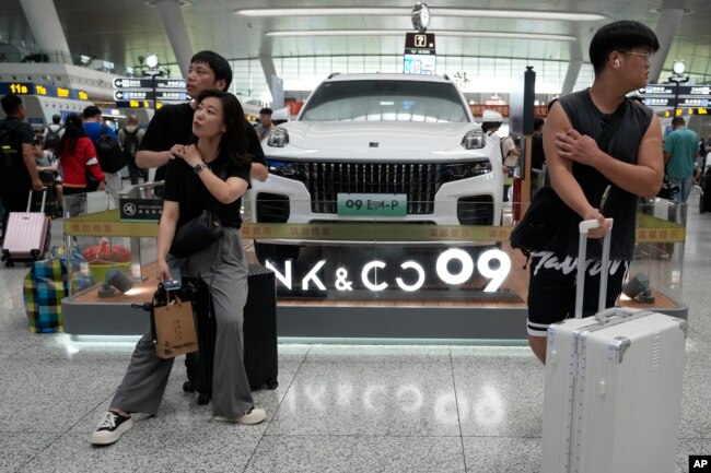 FILE - Passengers wait near a hybrid luxury SUV from China automaker Lynk&co displayed at the train station in Hangzhou in eastern China's Zhejiang province on Monday, July 3, 2023. (AP Photo/Ng Han Guan, File)