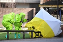 FILE - Members of the emergency services in biohazard suits afix a tent over the bench where former Russian spy Sergei Skripal and his daughter were found March 4 in critical condition, in Salisbury, southern England, on March 8, 2018.