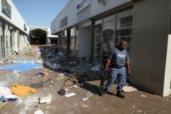 FILE - A police officer stands on the street, next to vandalized and looted stores, as protests continue following imprisonment of former South Africa President Jacob Zuma, in Katlehong, South Africa, July 12, 2021.