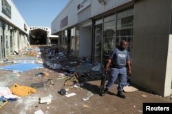 FILE - A police officer stands on the street, next to vandalized and looted stores, as protests continue following imprisonment of former South Africa President Jacob Zuma, in Katlehong, South Africa, July 12, 2021.