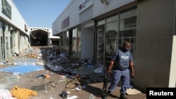 A police officer stands on the street, next to vandalized and looted stores, as protests continue following imprisonment of former South Africa President Jacob Zuma, in Katlehong, South Africa, July 12, 2021. 
