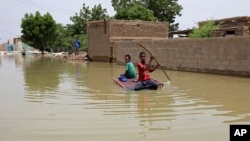 FILE - Young boys navigate a flooded street on a makeshift raft through the town of Salmaniya, about 25 miles (35 km) southwest of the capital, Khartoum, Sudan, Sept. 17, 2020. 