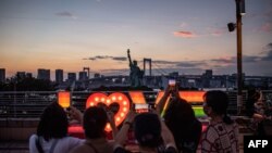 La gente toma fotografías de una réplica de la Estatua de la Libertad en el paseo marítimo de Odaiba en Tokio el 22 de julio de 2021, en vísperas del inicio de los Juegos Olímpicos de Tokio 2020. (Foto de Philip FONG / AFP)