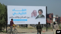 Iraqis walk by a poster announcing the upcoming visit of Pope Francis and his planned meeting with prominent Shiite Muslim leader, Ayatollah Ali al-Sistani, in Najaf, Iraq, March 3, 2021.